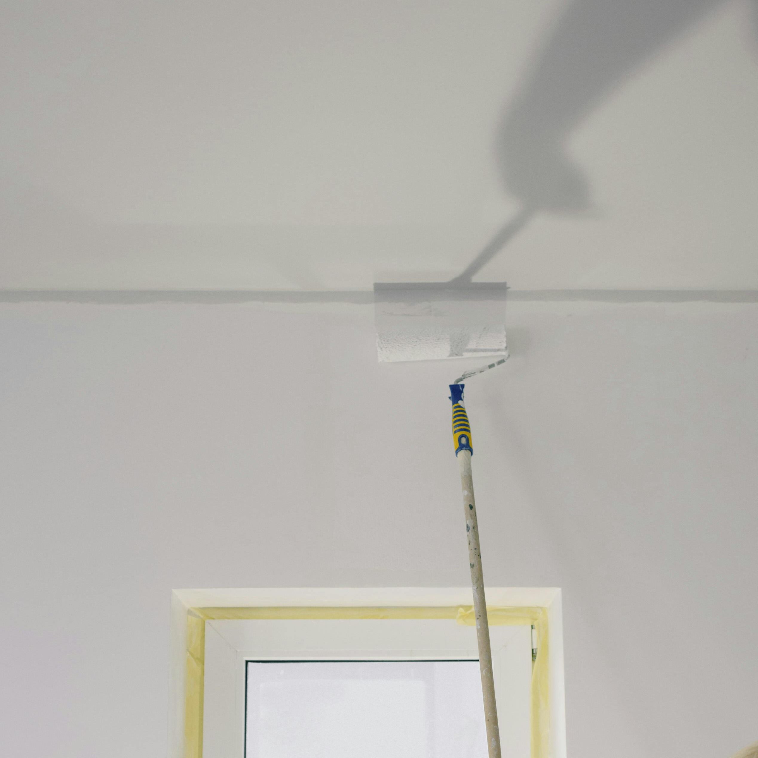 Crop faceless female holding paint roller and renovating walls in room at home